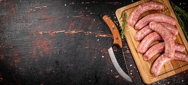 Фото Сырые сосиски на разделочной доске с ножом и розмарином