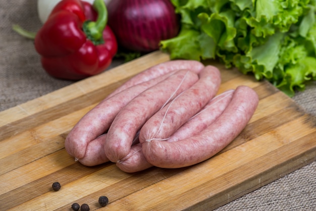 Raw sausages with vegetables on wooden cutting board