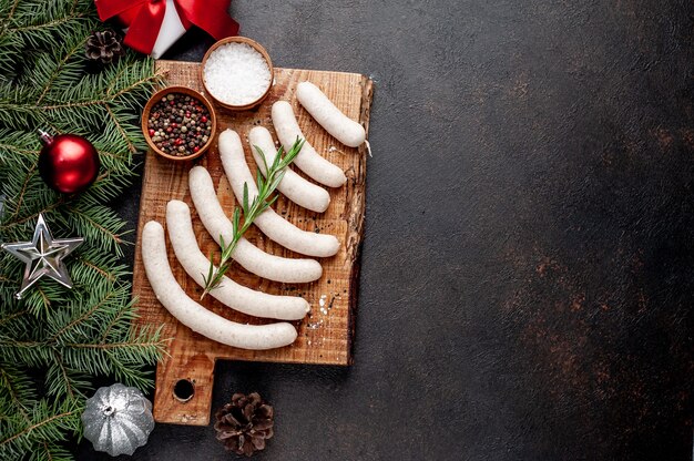 Raw sausages on wooden board with Christmas decorations beside