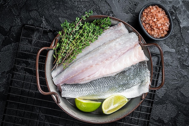 Raw Sea Bass fillet Labrax fish with herbs and lime Black background Top view