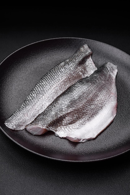 Raw sea bass fish fillet with salt spices and herbs on a ceramic plate