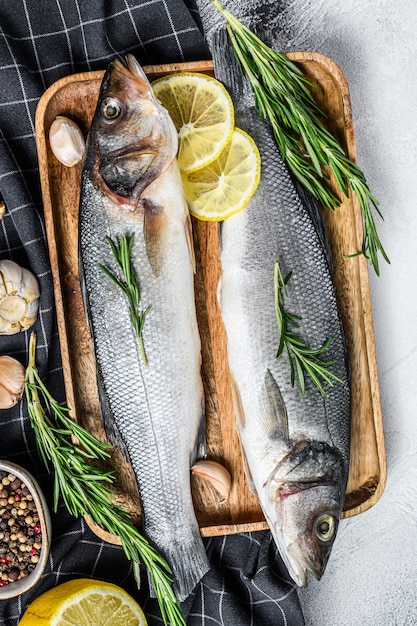 Raw sea bass fish with herbs and lemon on Black table. 