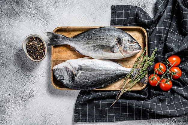 Raw sea bream fish with cooking ingredients, cherry tomatoes, thyme, pepper. Gray background. top view
