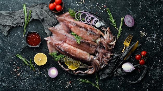 Il calamaro crudo su una lastra di pietra nera è pronto per essere cucinato vista dall'alto su uno sfondo scuro