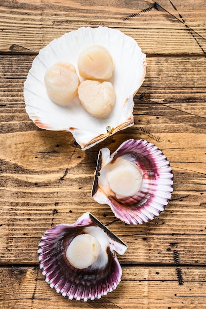 Raw seafood scallops meat on a shells. Wooden background. Top view.