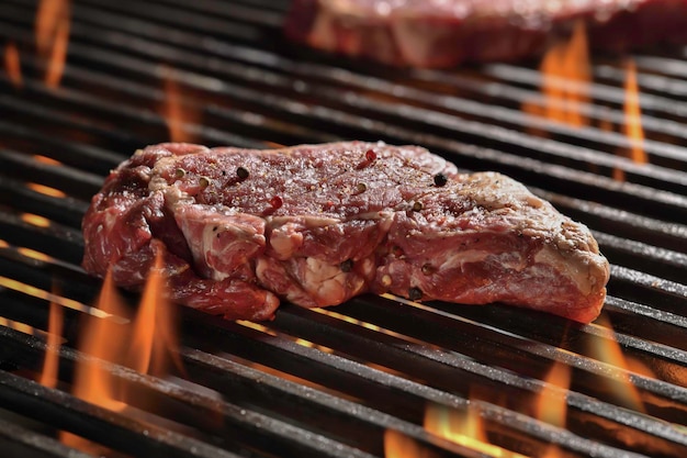 Raw seansoned ribeye steaks meat beef cooking on flaming grill