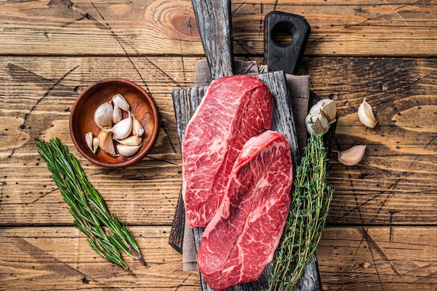 Raw Shoulder Top Blade  beef meat steaks on a wooden butcher board with herbs. wooden background. Top View.