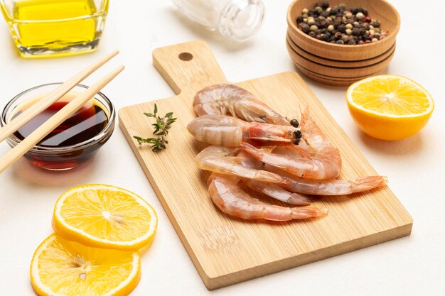 Raw shrimp on cutting board Lemon slices allspice in wooden bowl Soy sauce in bowl and chopsticks Top view White background