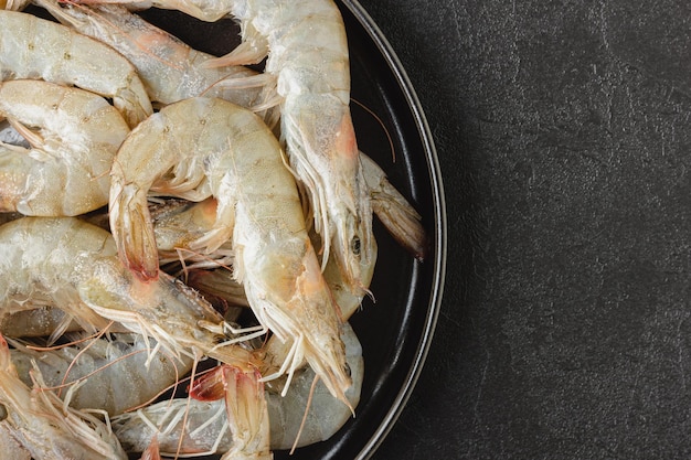 Raw shrimps on black plate. Uncooked seafood on dark background with copy space. Top view.