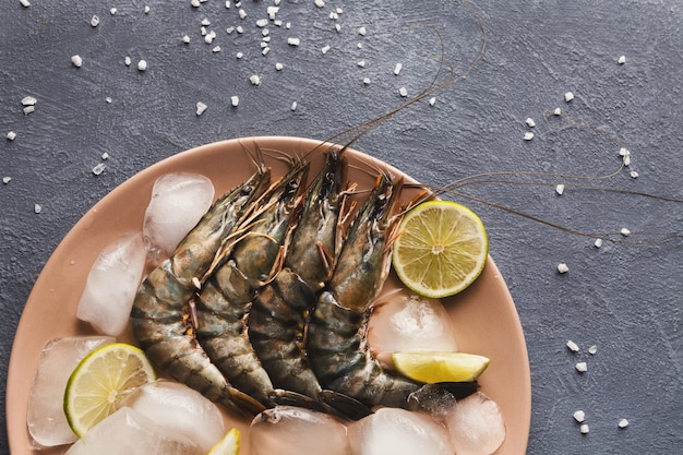 Raw shrimps with lemon and ice cubes on light plate, copy space on gray background. Top view on appetizing seafood snack, restaurant serving, copy space