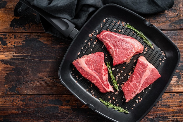 Raw sirloin beef steak Rump steak cut on a grill skillet Wooden background Top view Copy space