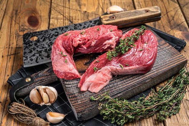Lembo di controfiletto crudo o bistecca di carne di manzo cruda bavette su una tavola da macellaio in legno con mannaia di carne sfondo in legno vista dall'alto