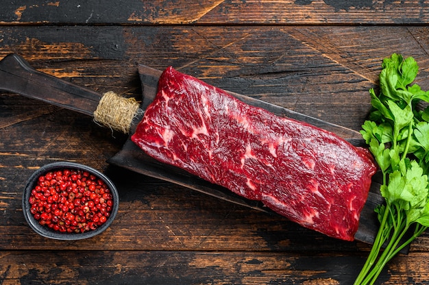 Raw skirt or machete beef meat steak on a cutting board. Dark wooden table. Top view.