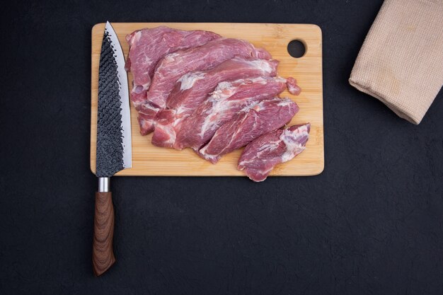 Raw sliced meat lies on a wooden Board and a black table with a beautiful chefs knife