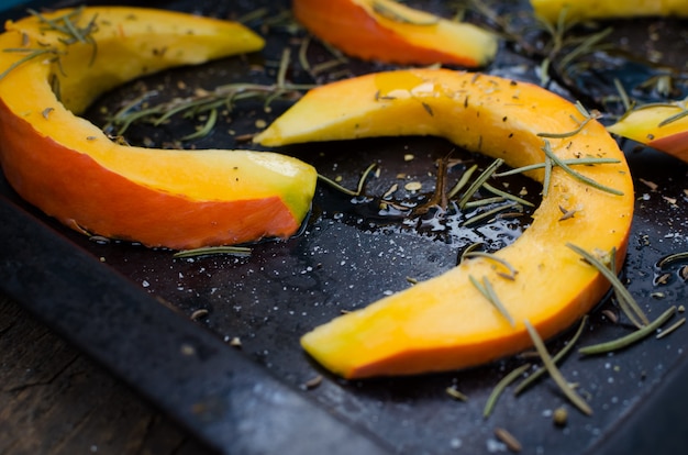 Raw sliced pumpkin on a baking tray with rosemary