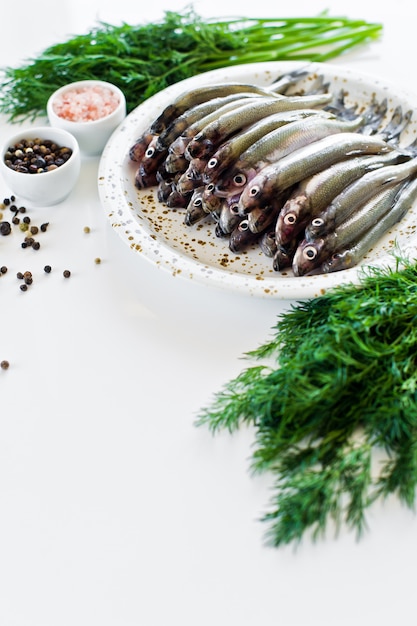 Photo raw smelt on a plate, dill, pink salt, pepper and garlic.