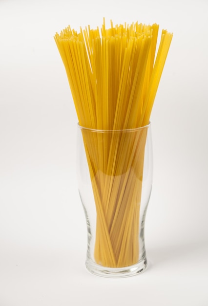 Сырые макароны спагетти в стакане на белом фоне