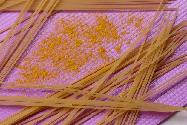 Raw spaghetti with yellow spices on a purple background Closeup of an Italian pasta View from above