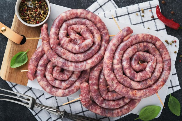 Salsicce di maiale a spirale crude salsicce di maiale fresche gustose spirali attorcigliate per barbecue su supporto bianco con spezie ed erbe aromatiche per la cena di festa dell'oktoberfest su sfondo grigio vista dall'alto set dell'oktoberfest