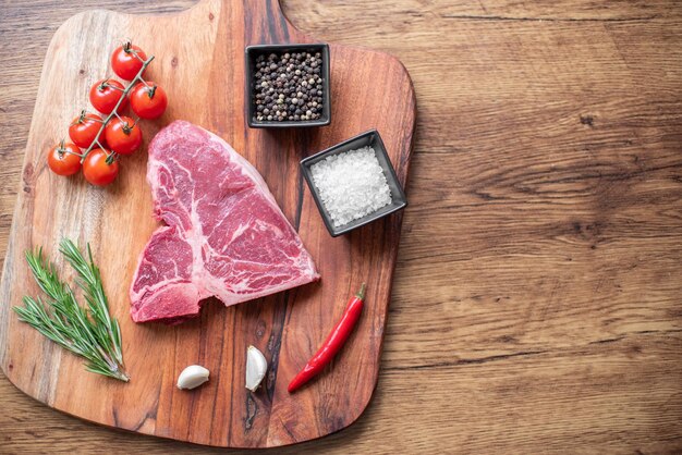 raw steak on a cutting board with herbs. Wooden background.