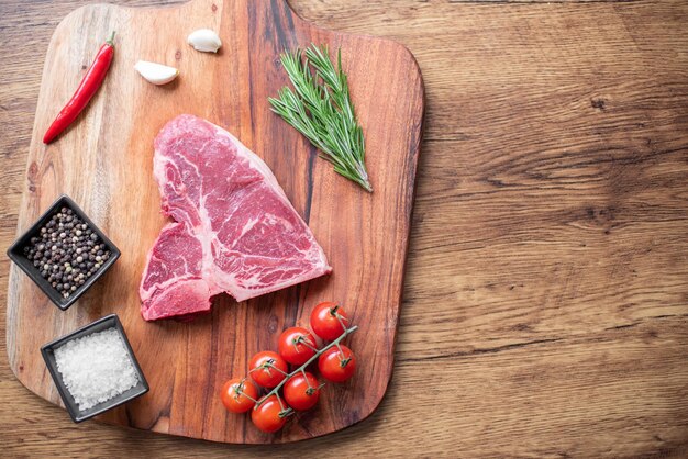 raw steak on a cutting board with herbs. Wooden background.