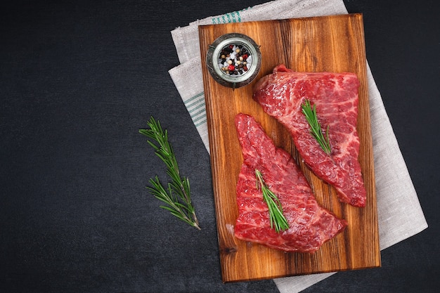 Raw steak on cutting board with rosemary and spices