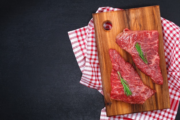 Raw steak on cutting board with rosemary and spices