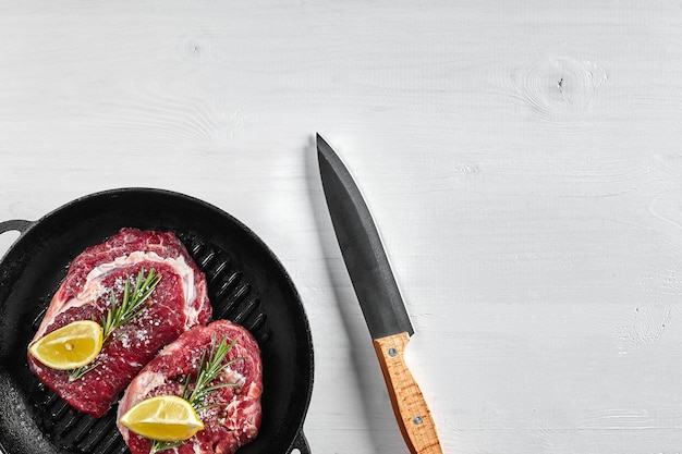 Raw Steak in grill frying pan with herbs and oil on white background top view place for text