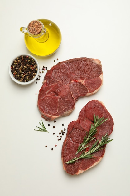 Raw steak meat, herbs, spices and oil on white table