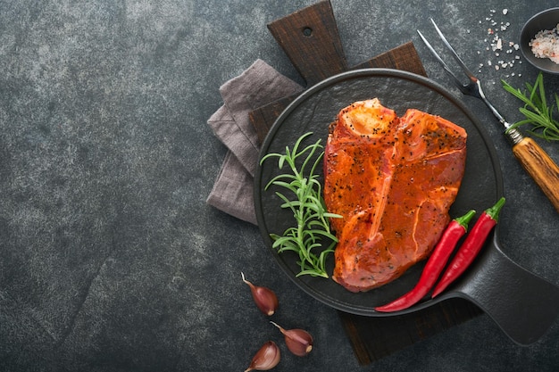 Raw steak tbone or porterhouse Steak tbone or porterhouse in sauce with spices salt and rosemary on a black ceramic plate on concrete background Top view Place for text