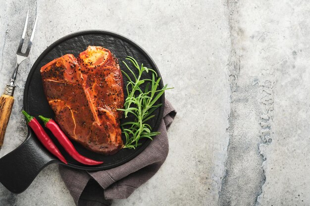 Raw steak tbone or porterhouse Steak tbone or porterhouse in sauce with spices salt and rosemary on a black ceramic plate on concrete background Top view Place for text