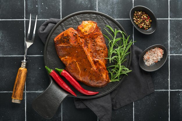 Raw steak tbone or porterhouse Steak tbone or porterhouse in sauce with spices salt and rosemary on a black ceramic plate on concrete background Top view Place for text