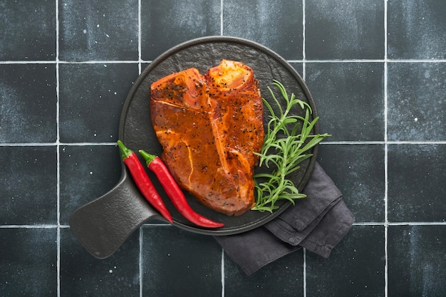 Raw steak tbone or porterhouse Steak tbone or porterhouse in sauce with spices salt and rosemary on a black ceramic plate on concrete background Top view Place for text