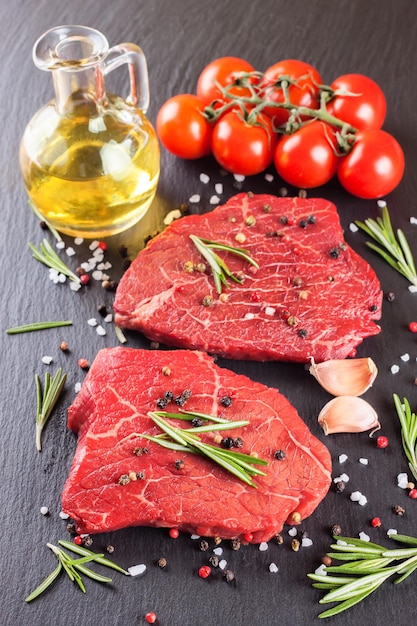 Raw steak with cooking ingridients on black slate background