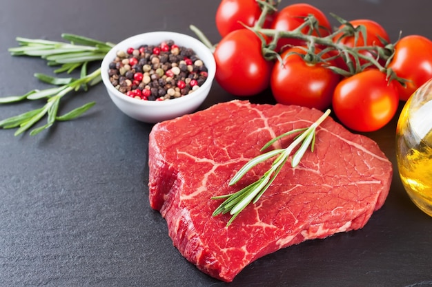 Raw steak with cooking ingridients on black slate background