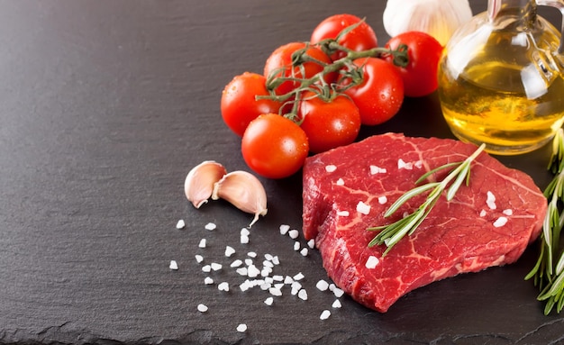 Raw steak with cooking ingridients on black slate background