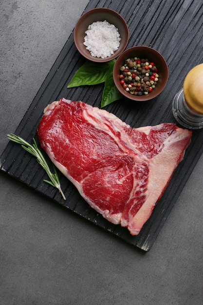 Raw steak with spices on cutting board