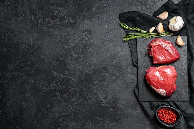 Raw steaks fillet Mignon prepared for cooking. Beef tenderloin. Black background. Top view. Space for text