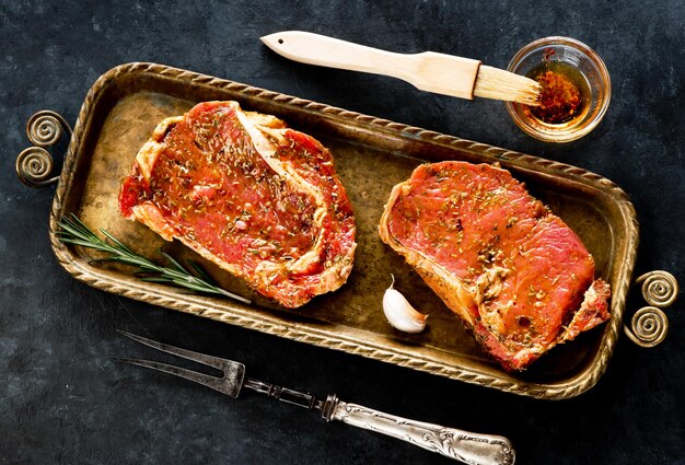 Raw steaks ribeye with garlic and rosemary and a vintage mental fork