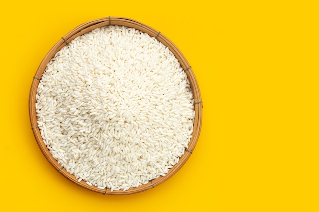 Raw sticky rice in bamboo basket on yellow background