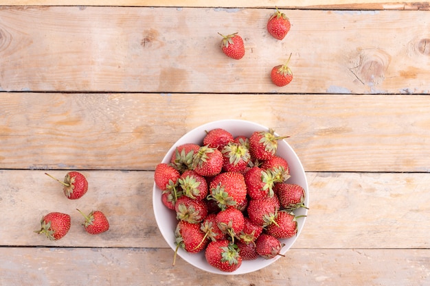 Raw strawberries in plate on wooden table,top view