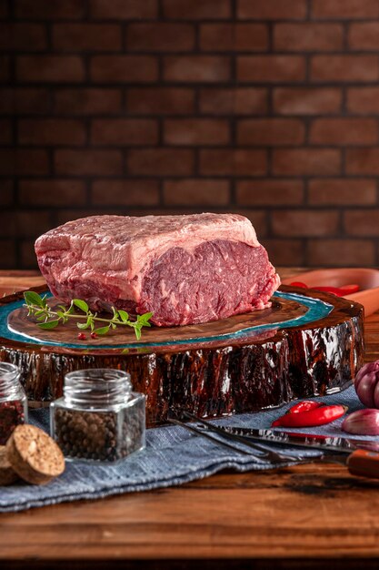 Raw strip loin beef (argentine chorizo) on a wood resined cutting board with spices. Wooden table with bricks wall background.