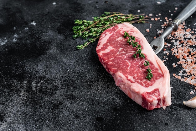 Photo raw striploin steak on a butcher table with salt and thyme. black background. top view. copy space.