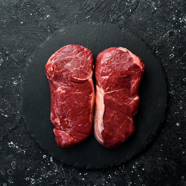 Raw striploin steak New York of beef on a board Top view On a black stone plate