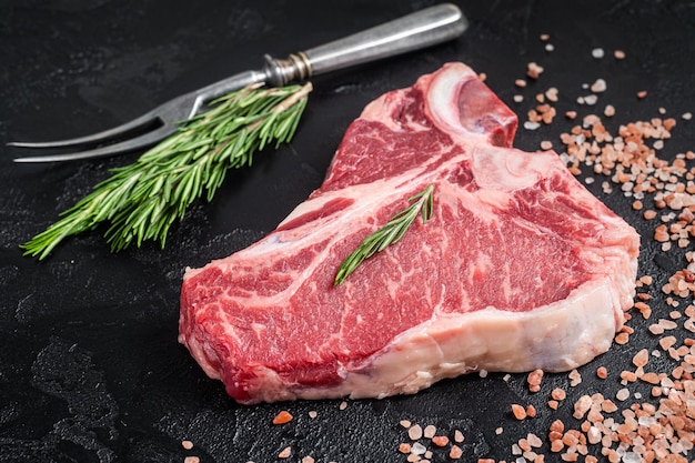 Raw T bone beef meat steak porterhouse steak on butcher table with rosemary Black background Top view