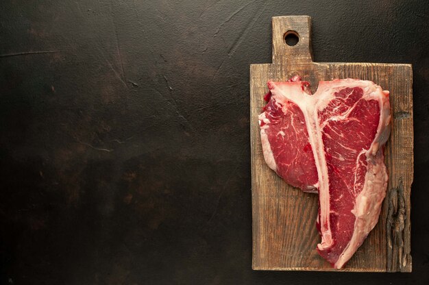 Raw t-bone steak met verse kruiden op een betonnen of leisteen achtergrond, bovenaanzicht, plaats voor tekst,