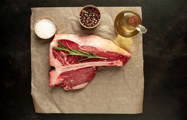 Raw t-bone steak with fresh herbs on a concrete or slate background