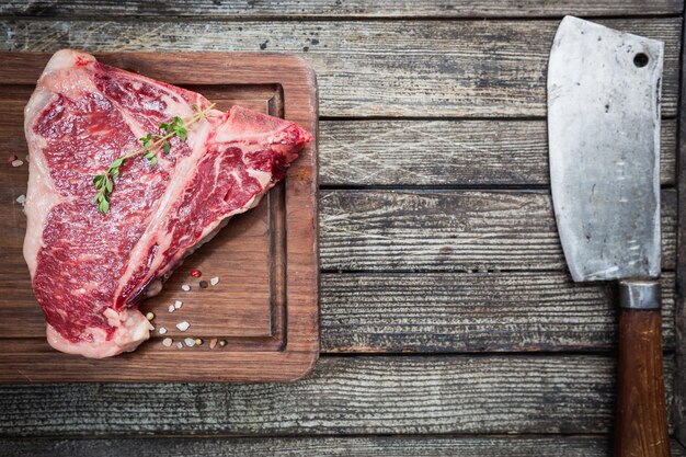 Raw T-bone Steak with fresh herbs and oil on dark wooden background, top view