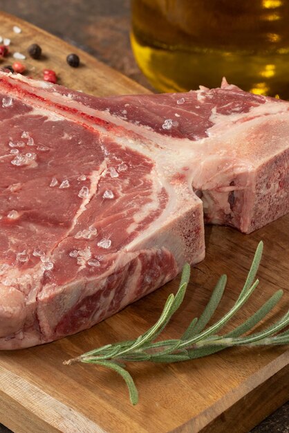 Raw T bone steak with rosemary and black pepper