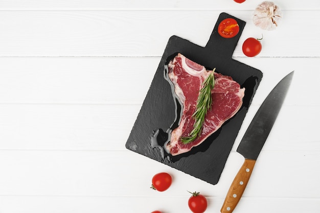 Raw t-bone steak on wooden cutting board on wooden table close up